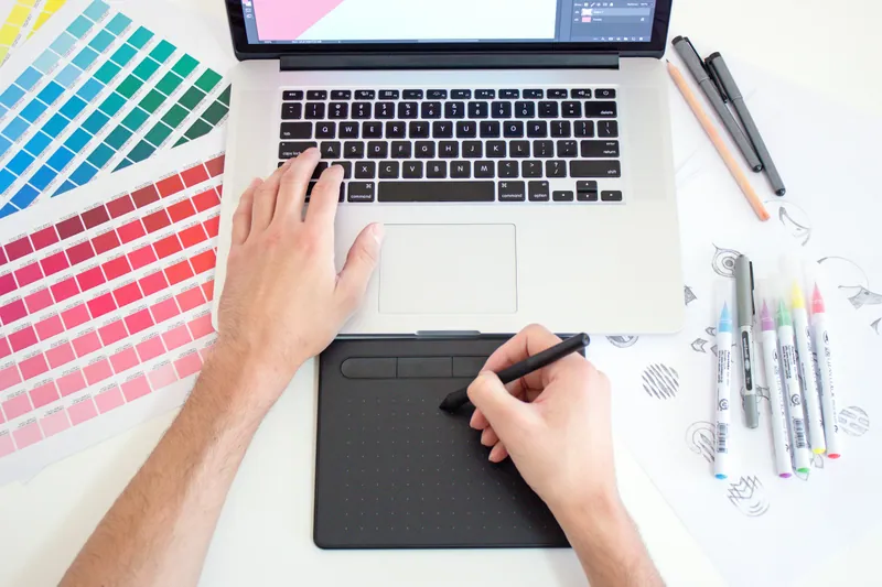 Mains dessinant sur une tablette graphique à côté d'un ordinateur portable