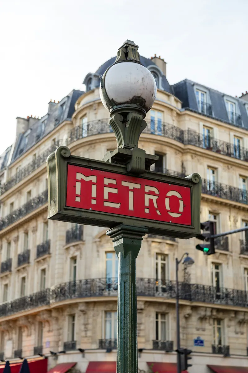 Enseigne rouge du métro parisien devant un immeuble haussmannien